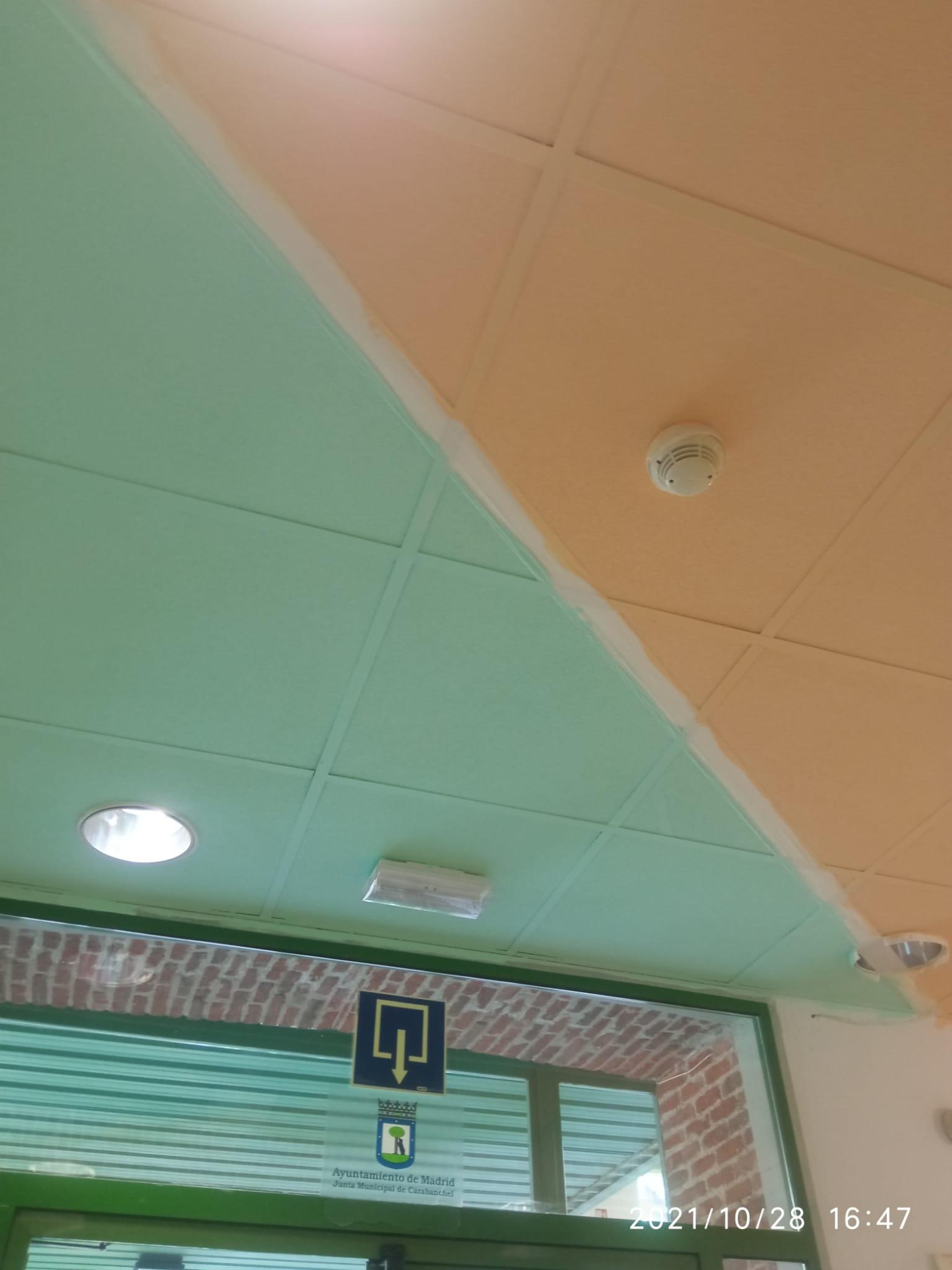 Techo bicolor en centro para mayores: verde y beige, con iluminación y señalización. Salida marcada con flecha amarilla sobre fondo azul. Diseño facilita orientación espacial y seguridad.